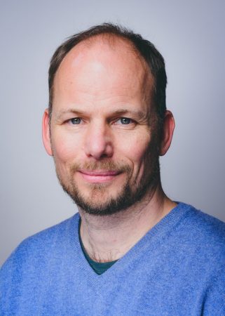 Portraitaufnahme von Philipp Wetzel. Er trägt einen hellblauen Pullover und lächelt in die Kamera.
